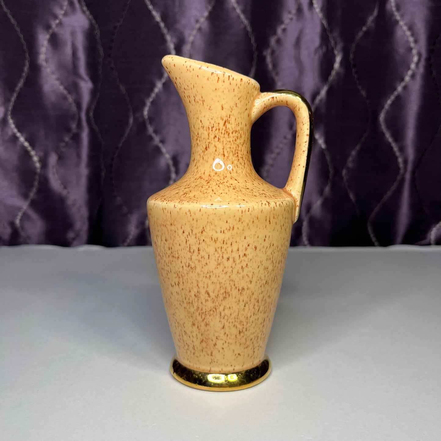 Small ceramic pitcher, tan with brown specks and gold trim, 7 inches tall