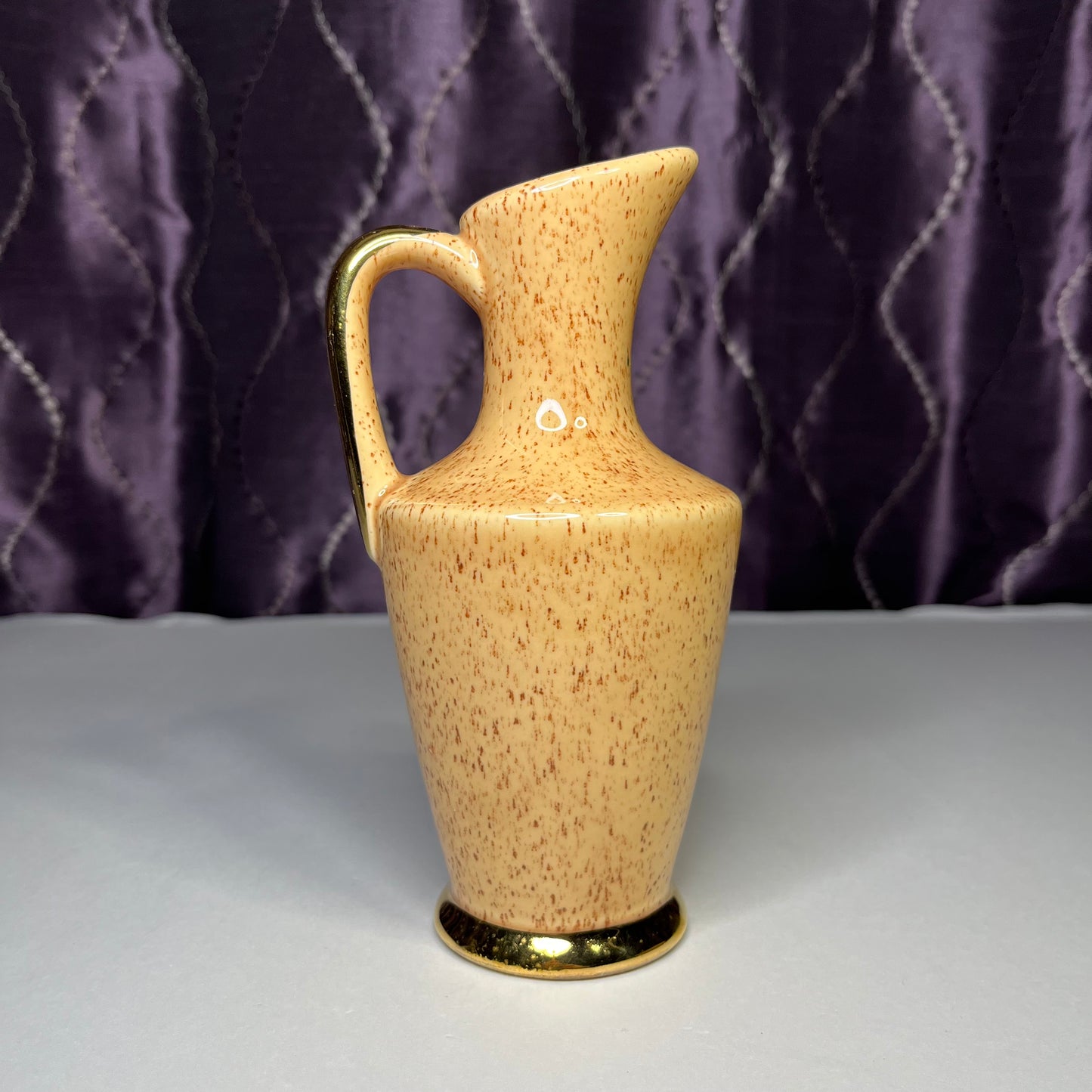 Small ceramic pitcher, tan with brown specks and gold trim, 7 inches tall